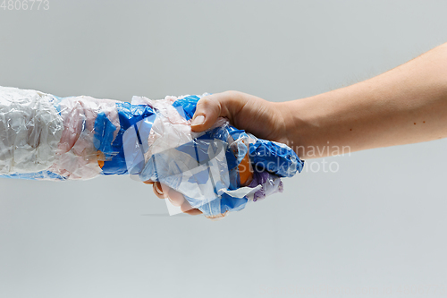 Image of Big plastic hand made of garbage shaking another hand isolated on white studio background