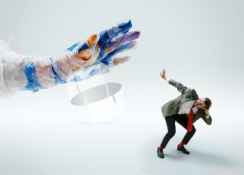 Image of Young caucasian man avoiding big plastic hand on white studio background