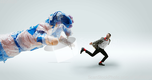 Image of Young caucasian man avoiding big plastic hand on white studio background