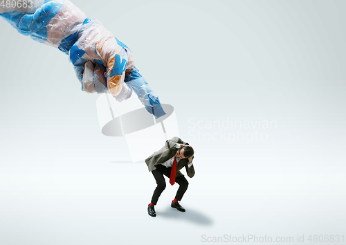 Image of Young caucasian man avoiding big plastic hand on white studio background