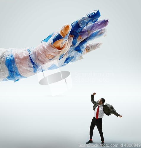 Image of Young caucasian man avoiding big plastic hand on white studio background