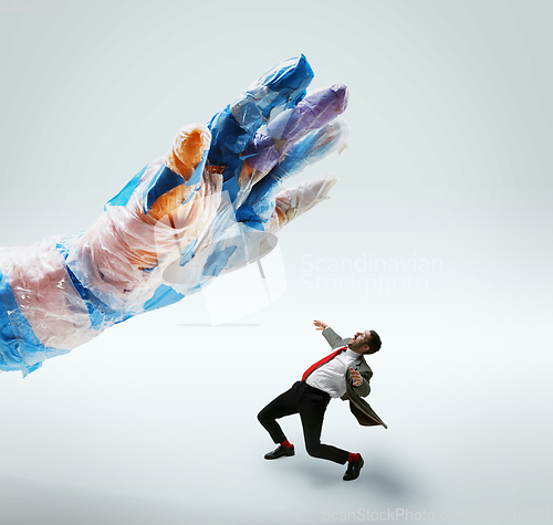 Image of Young caucasian man avoiding big plastic hand on white studio background