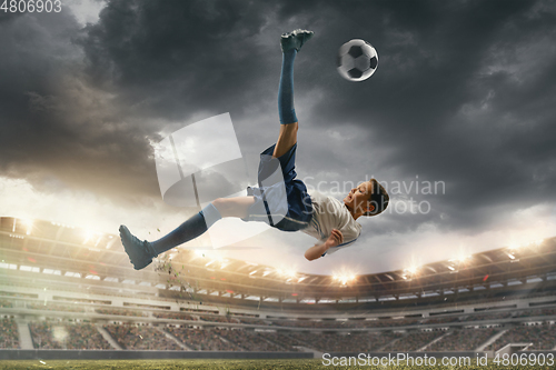 Image of Young male soccer player kicking ball on stadium with flashlights on background