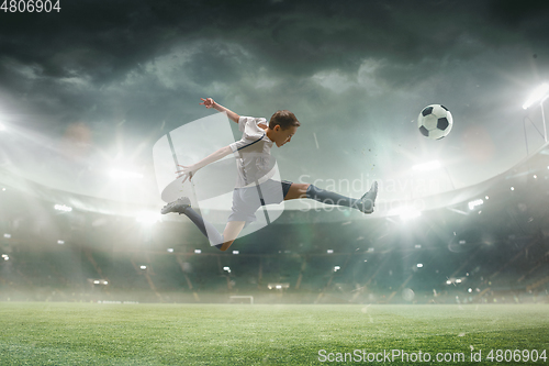 Image of Young male soccer player kicking ball on stadium with flashlights on background