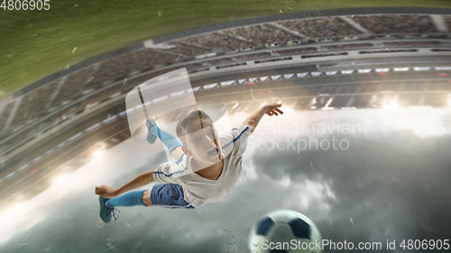 Image of Young male soccer player kicking ball on stadium with flashlights on background