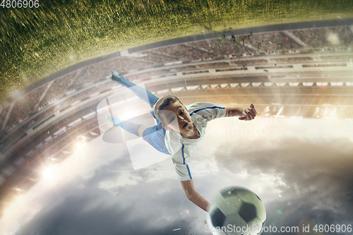 Image of Young male soccer player kicking ball on stadium with flashlights on background