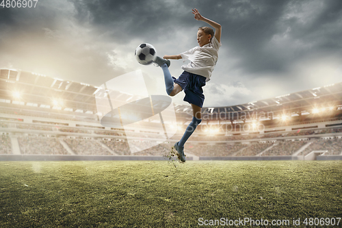 Image of Young male soccer player kicking ball on stadium with flashlights on background
