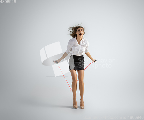 Image of Caucasian woman in office clothes jumping with rope isolated on grey studio background