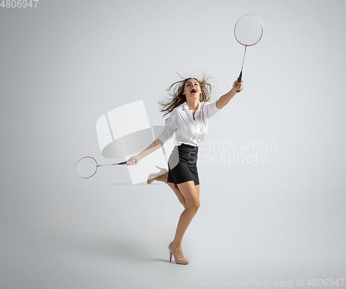 Image of Caucasian woman in office clothes plays badminton isolated on grey studio background