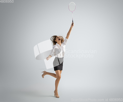 Image of Caucasian woman in office clothes plays badminton isolated on grey studio background