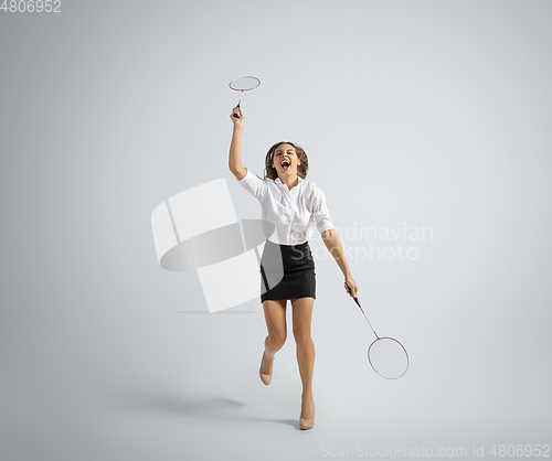 Image of Caucasian woman in office clothes plays badminton isolated on grey studio background