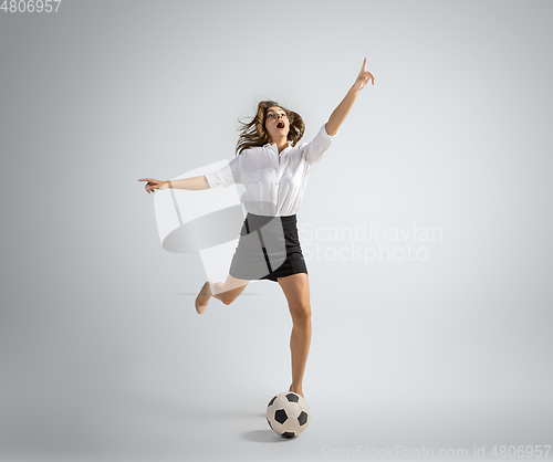 Image of Caucasian woman in office clothes kicking ball isolated on grey studio background