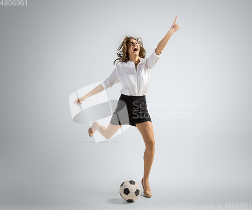 Image of Caucasian woman in office clothes kicking ball isolated on grey studio background