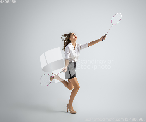 Image of Caucasian woman in office clothes plays badminton isolated on grey studio background