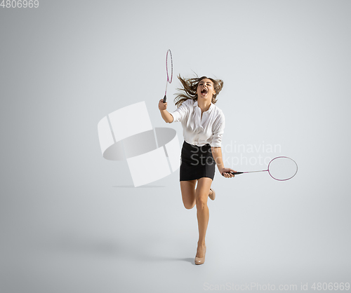 Image of Caucasian woman in office clothes plays badminton isolated on grey studio background