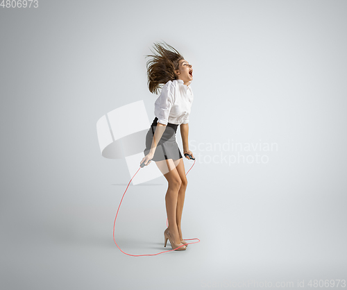 Image of Caucasian woman in office clothes jumping with rope isolated on grey studio background