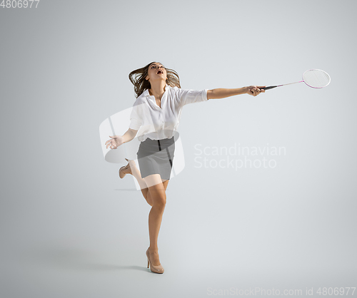 Image of Caucasian woman in office clothes plays badminton isolated on grey studio background