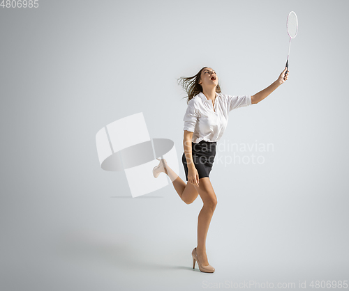 Image of Caucasian woman in office clothes plays badminton isolated on grey studio background