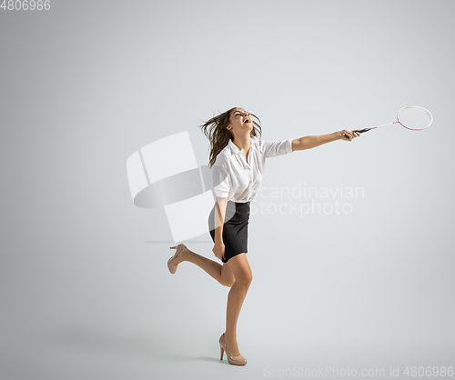 Image of Caucasian woman in office clothes plays badminton isolated on grey studio background