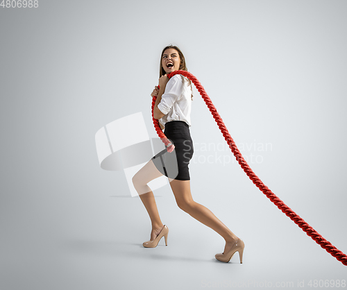 Image of Caucasian woman in office clothes training with ropes isolated on grey studio background