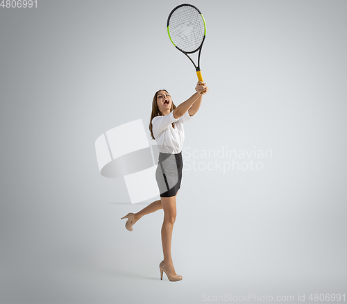 Image of Caucasian woman in office clothes plays tennis isolated on grey studio background