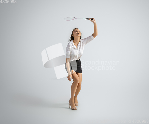 Image of Caucasian woman in office clothes plays badminton isolated on grey studio background