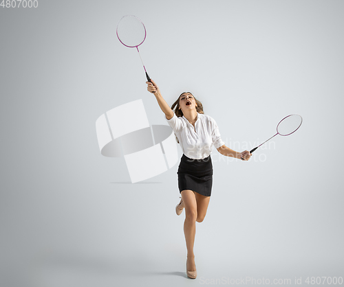 Image of Caucasian woman in office clothes plays badminton isolated on grey studio background