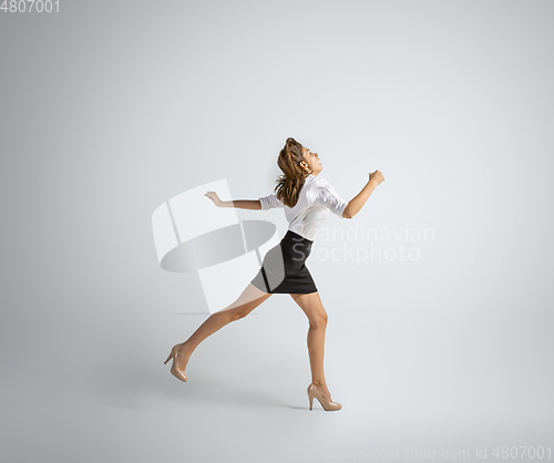 Image of Caucasian woman in office clothes running isolated on grey studio background