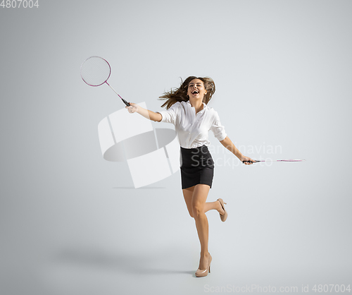 Image of Caucasian woman in office clothes plays badminton isolated on grey studio background