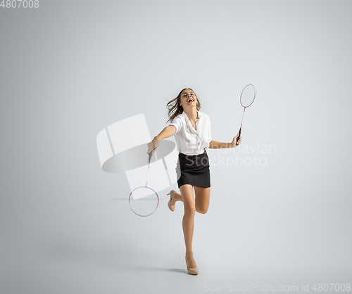 Image of Caucasian woman in office clothes plays badminton isolated on grey studio background