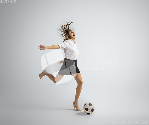 Image of Caucasian woman in office clothes kicking ball isolated on grey studio background