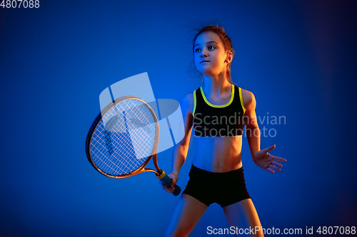 Image of Little caucasian girl playing tennis isolated on blue background in neon light