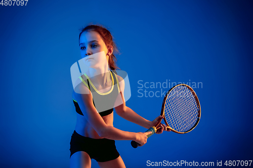 Image of Little caucasian girl playing tennis isolated on blue background in neon light