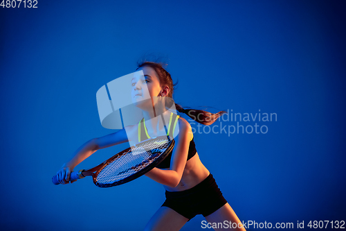 Image of Little caucasian girl playing tennis isolated on blue background in neon light