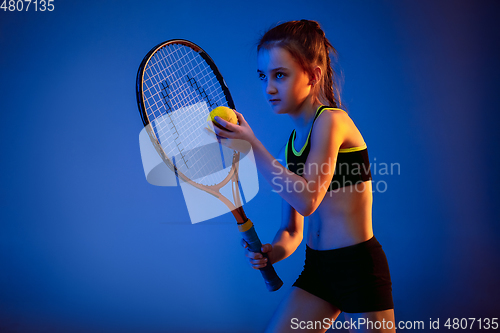 Image of Little caucasian girl playing tennis isolated on blue background in neon light