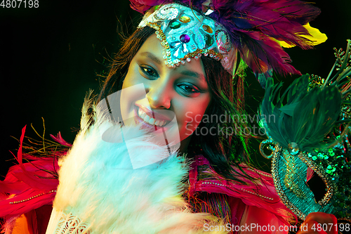 Image of Beautiful young woman in carnival mask and masquerade costume in colorful lights