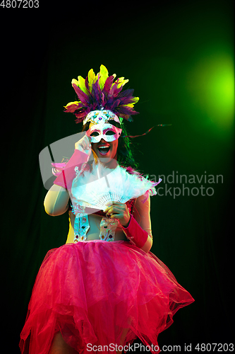 Image of Beautiful young woman in carnival mask and masquerade costume in colorful lights