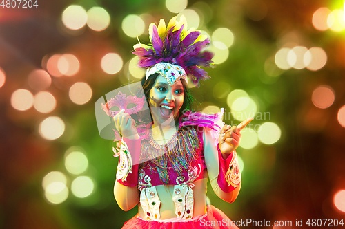 Image of Beautiful young woman in carnival mask and masquerade costume in colorful lights