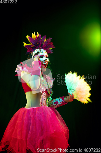 Image of Beautiful young woman in carnival mask and masquerade costume in colorful lights