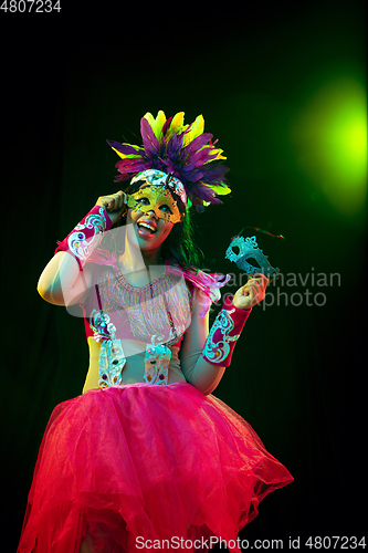 Image of Beautiful young woman in carnival mask and masquerade costume in colorful lights