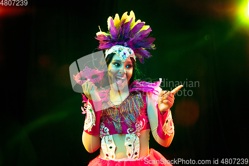 Image of Beautiful young woman in carnival mask and masquerade costume in colorful lights