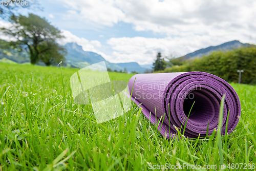 Image of Rolled up fitness mat on the green grass background