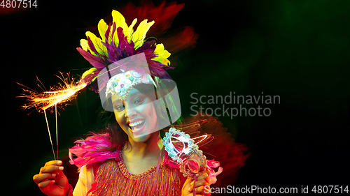 Image of Beautiful young woman in carnival mask and masquerade costume in colorful lights, flyer