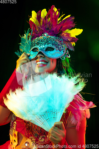 Image of Beautiful young woman in carnival mask and masquerade costume in colorful lights