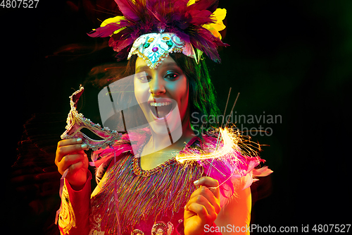 Image of Beautiful young woman in carnival mask and masquerade costume in colorful lights