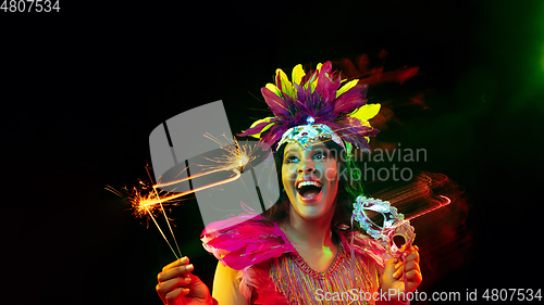 Image of Beautiful young woman in carnival mask and masquerade costume in colorful lights, flyer