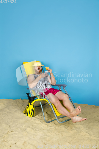 Image of Happy young man resting on blue studio background