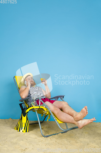 Image of Happy young man resting on blue studio background