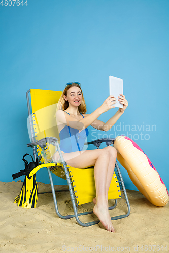 Image of Happy young woman resting on blue studio background