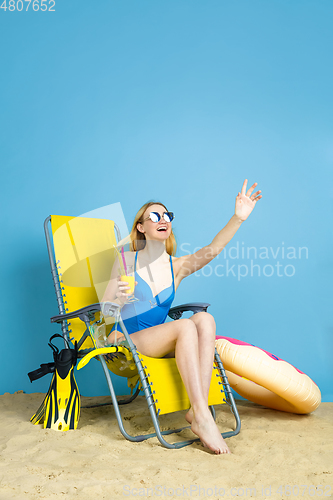 Image of Happy young woman resting on blue studio background